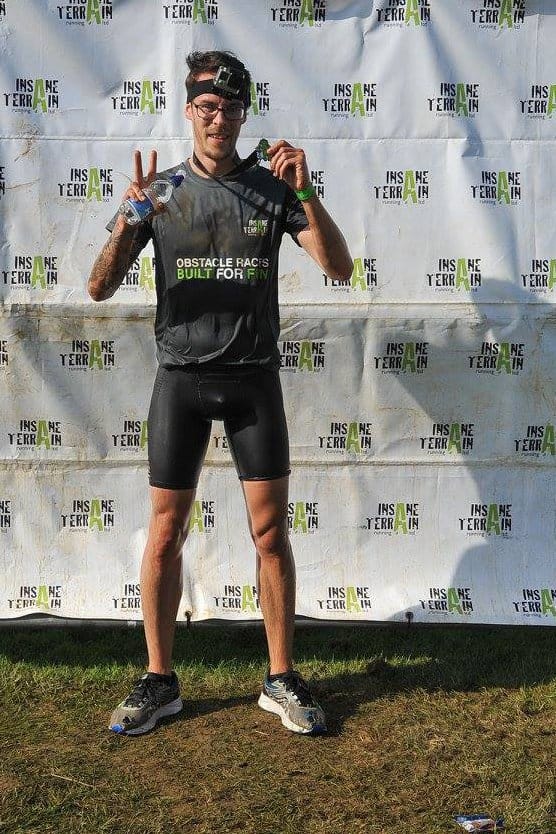 Carlos Eriksson posing in front of the Insane Terrain wall, medal in one hand and water in the other.